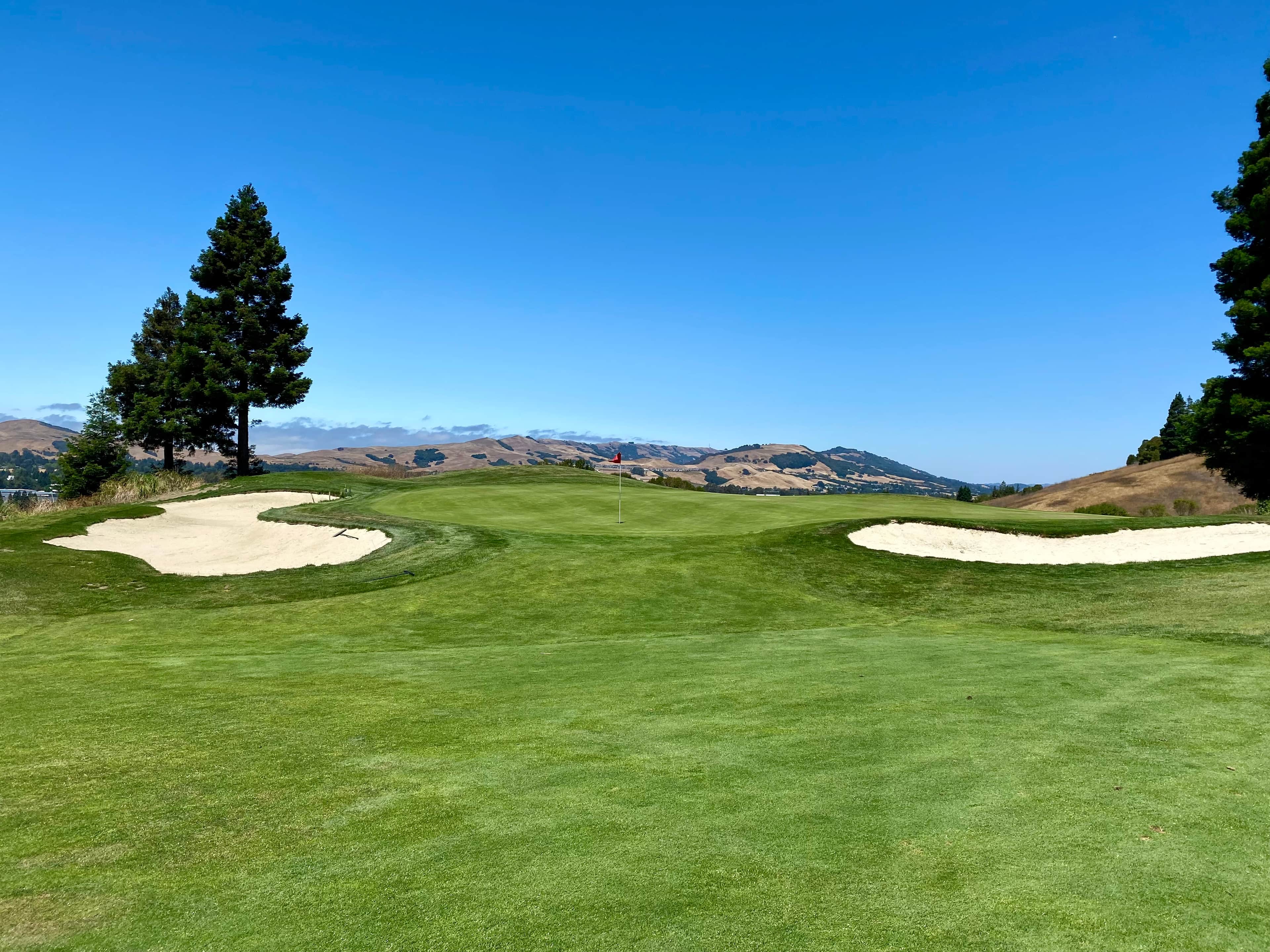 The 17th green flanked by bunkers, with trees and hills behind, at Canyon Lakes Golf Course in San Ramon, CA. Photo: official course site (canyonlakesgolfbrew.com)