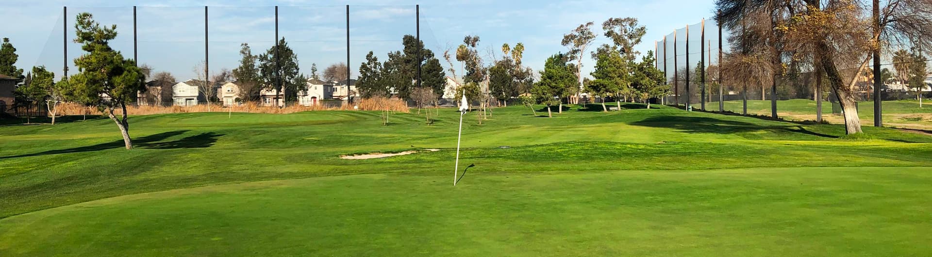 A manicured green with a flagstick at Rancho del Pueblo Golf Course in San Jose, California, with the driving range netting and neighborhood beyond. Photo courtesy of Rancho del Pueblo Golf Course (City of San Jose / CourseCo Golf Management), ranchodelpueblo.com.