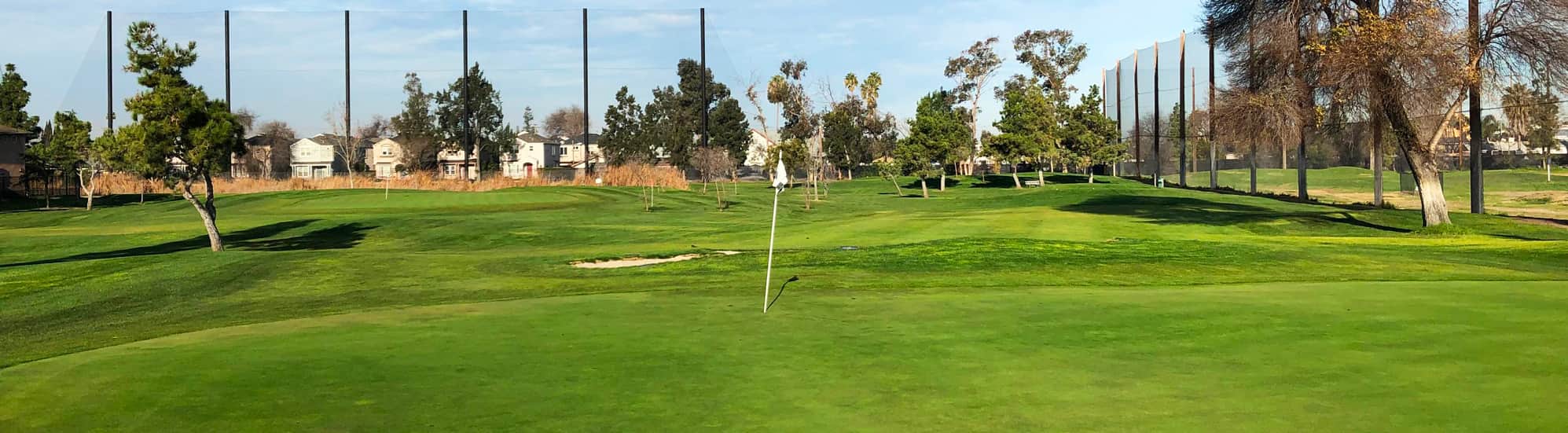 A manicured green with a flagstick at Rancho del Pueblo Golf Course in San Jose, California, with the driving range netting and neighborhood beyond. Photo courtesy of Rancho del Pueblo Golf Course (City of San Jose / CourseCo Golf Management), ranchodelpueblo.com.