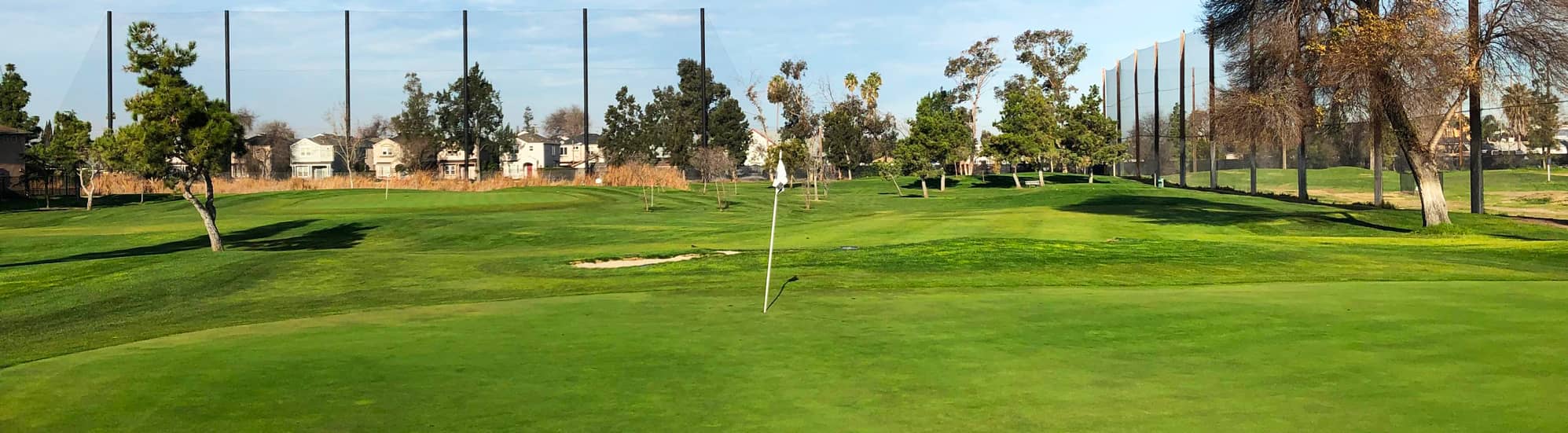 A manicured green with a flagstick at Rancho del Pueblo Golf Course in San Jose, California, with the driving range netting and neighborhood beyond. Photo courtesy of Rancho del Pueblo Golf Course (City of San Jose / CourseCo Golf Management), ranchodelpueblo.com.