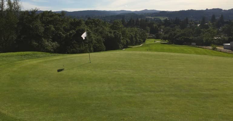 A hilltop green and flagstick at Healdsburg Golf Club at Tayman Park with views over the wooded valley and hills of Sonoma County. Photo credit: Pacific Coast Golf Guide (golfguide.net).