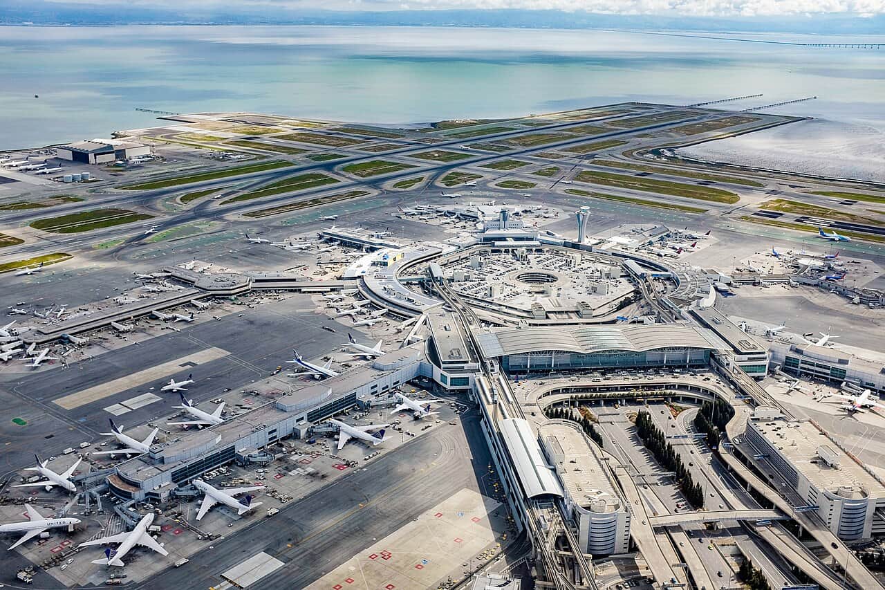 An aerial view of San Francisco International Airport's terminals and runways beside San Francisco Bay. Photo by Russss, 2015, licensed CC BY-SA 4.0, via Wikimedia Commons (File:San_Francisco_International_Airport_-_aerial_photo.jpg).